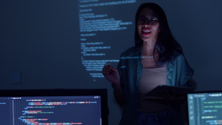 Young Asian woman software developers mentor leader manager talking to executive team analyzing source code in office at night. Programmer development concept.